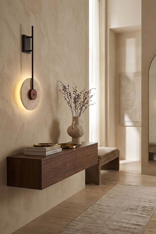 Lit travertine halo sconce on a beige wall | Travertine, Wood, Metal | Perspective view in a hallway over a wooden shelf | Samu Lamp