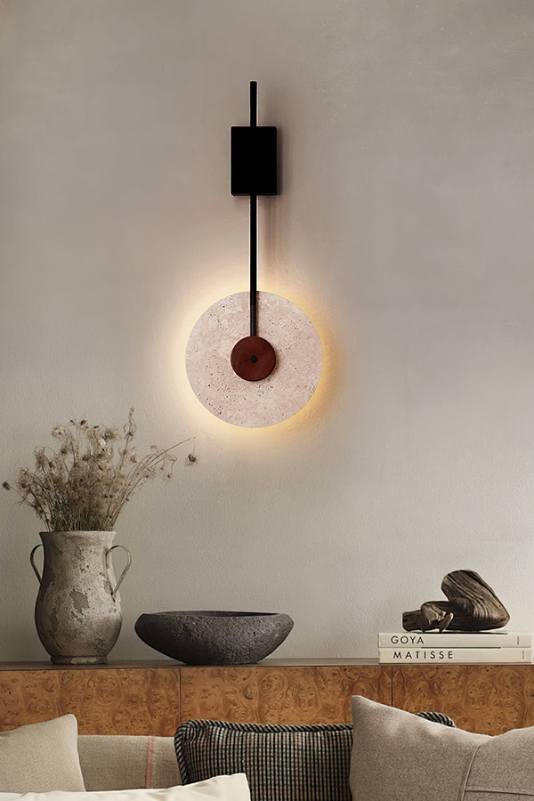 Travertine disk wall lamp above a decorative ledge | Travertine, Wood, Metal | Interior scene with ceramic vases and pillows | Samu Lamp