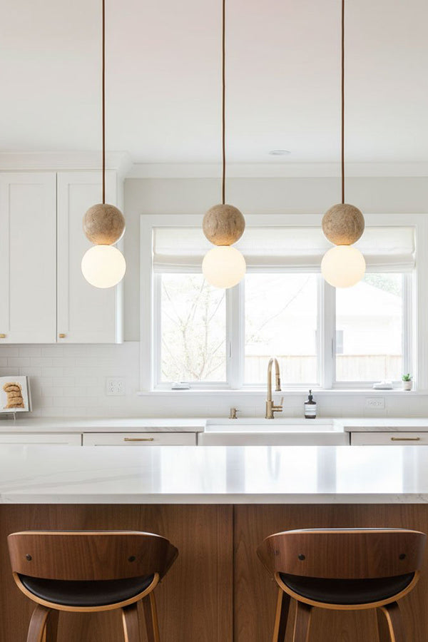Linear travertine pendant light arrangement | Yellow Travertine, Glass | Hanging over a white kitchen island with wooden stools | Samu Lamp