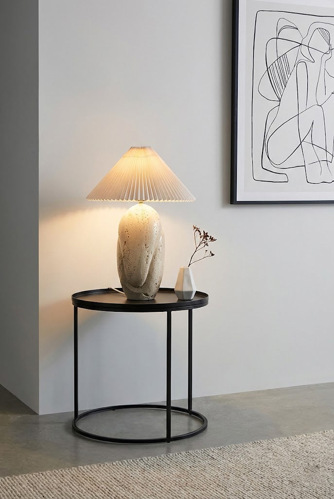Sculptural travertine lamp on metal stand | Travertine, Fabric | On a black round side table against a grey wall | Samu Lamp