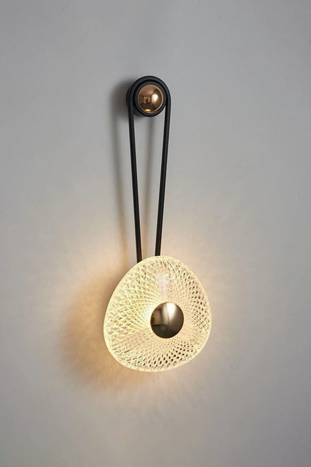Vara Aura Woven Acrylic Wall Lamp | Woven Acrylic, Brass | Fully illuminated wall sconce casting a warm, atmospheric glow against a neutral textured wall | Samu Lamp
