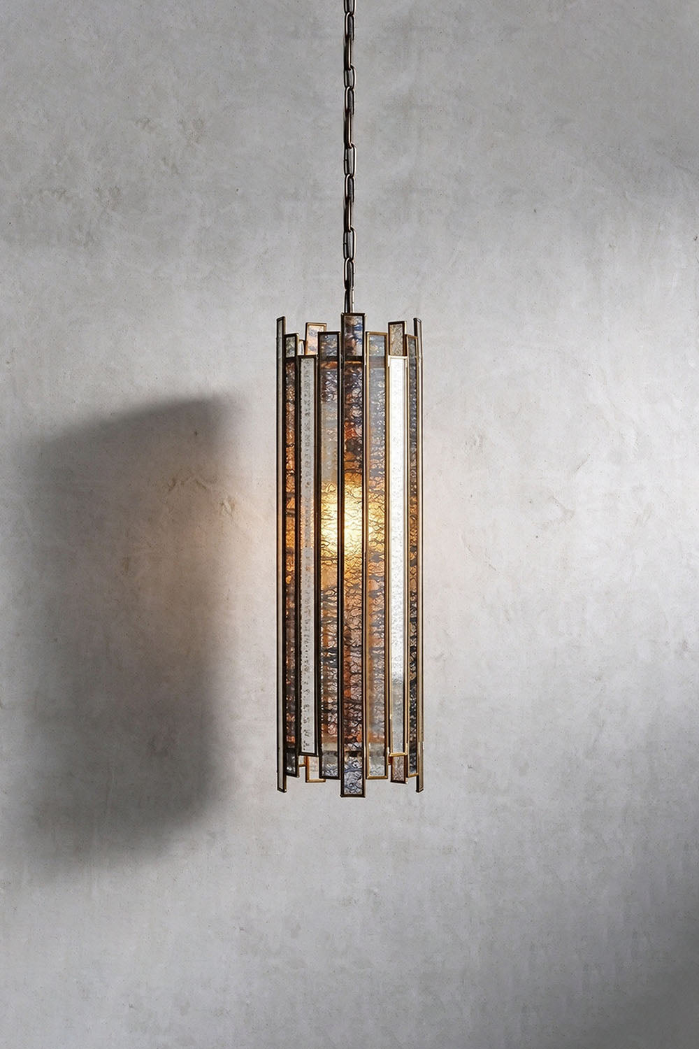 Vitrelle Cylinder Pendant | Textured Glass and Bronze | Front view illuminated against grey wall with warm glow | Samu Lamp