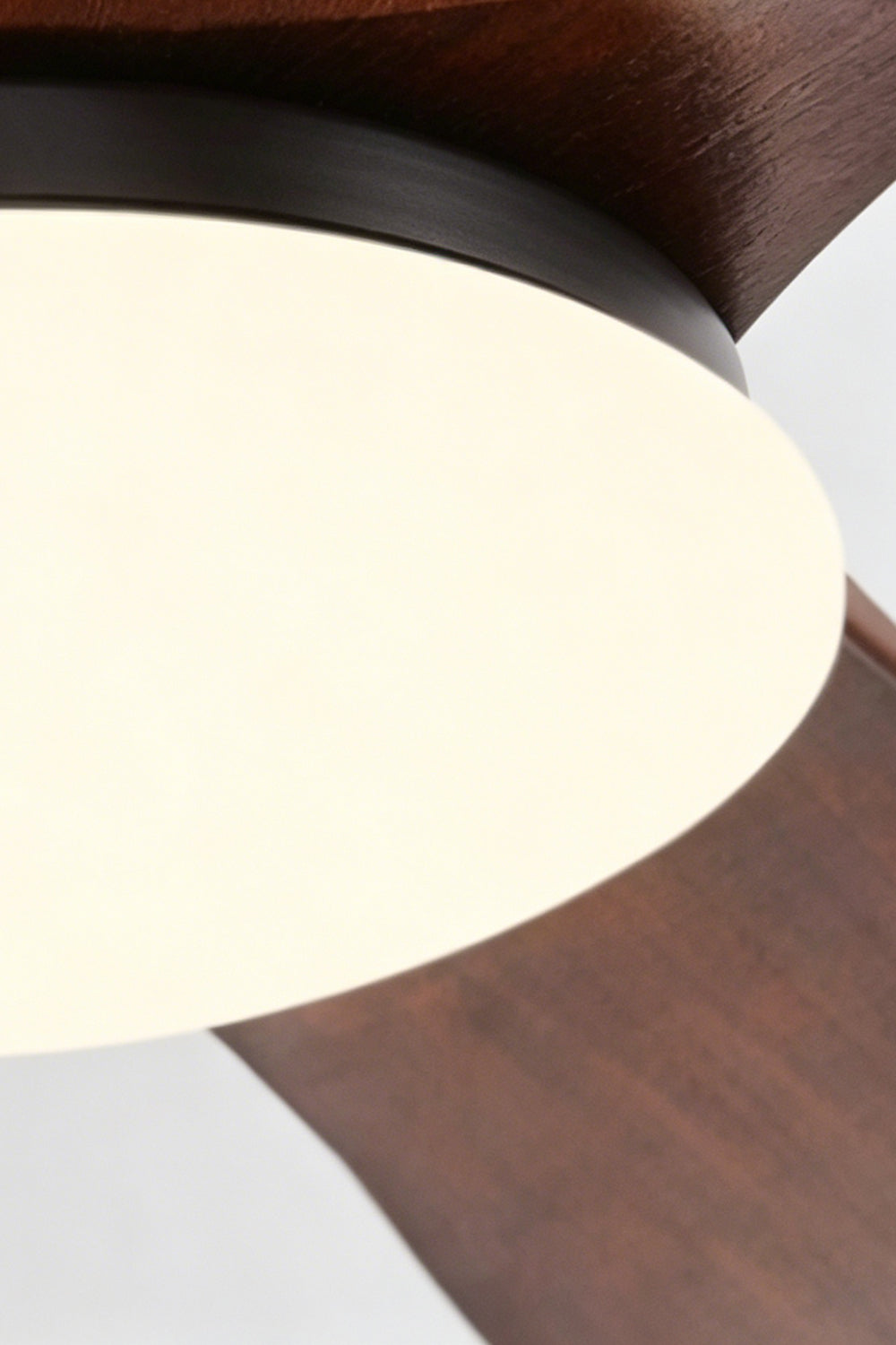 Volant Sculptural Wood Ceiling Fan Light | Wood, Metal | Close-up focus on the illuminated circular frosted glass diffuser panel and the matte black inner metallic trim ring | Detail shot | Samu Lamp