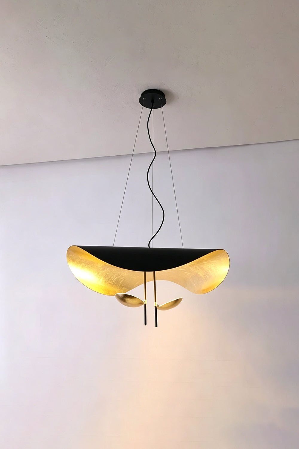Voluta Horizon Metal Pendant Light | Metal | Black and gold variant illuminated against a simple plain wall corner | Samu Lamp