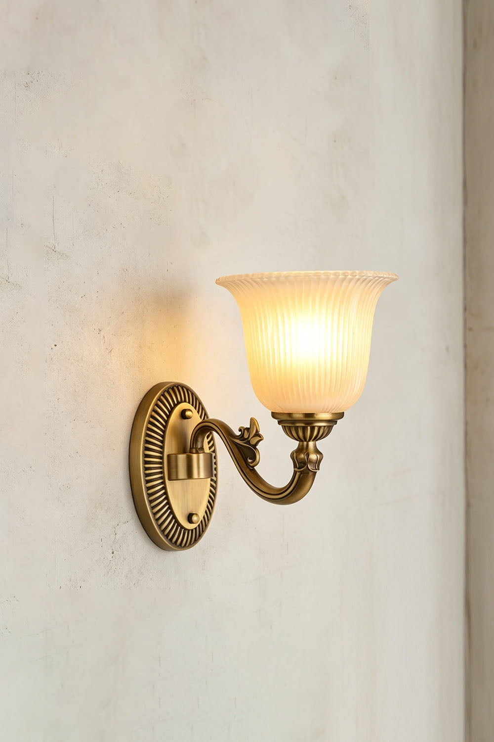 Whitlock Fluted Bell Brass Wall Lamp illuminating a textured wall with elegant design elements.