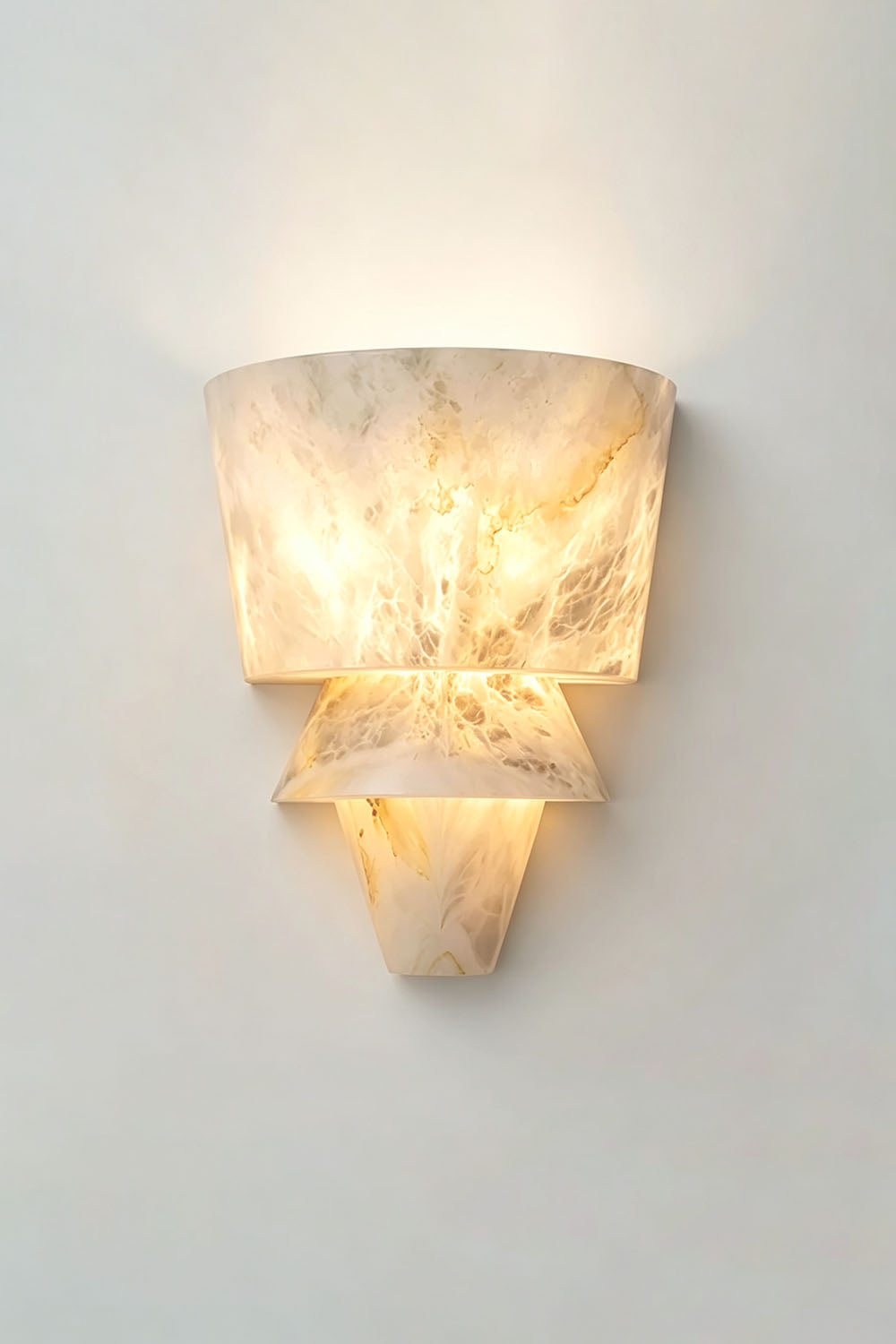 Wystan Twin Cone Alabaster Wall Lamp | Natural Alabaster and Metal | Studio shot showing the sconce casting a warm glow on a neutral wall | Samu Lamp