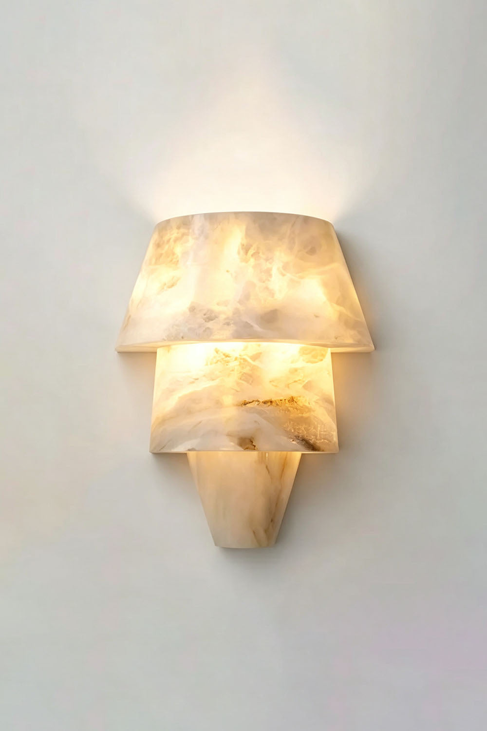 Wystan Twin Cone Alabaster Wall Lamp | Natural Alabaster and Metal | Angled product view illuminated softly on a neutral wall | Samu Lamp