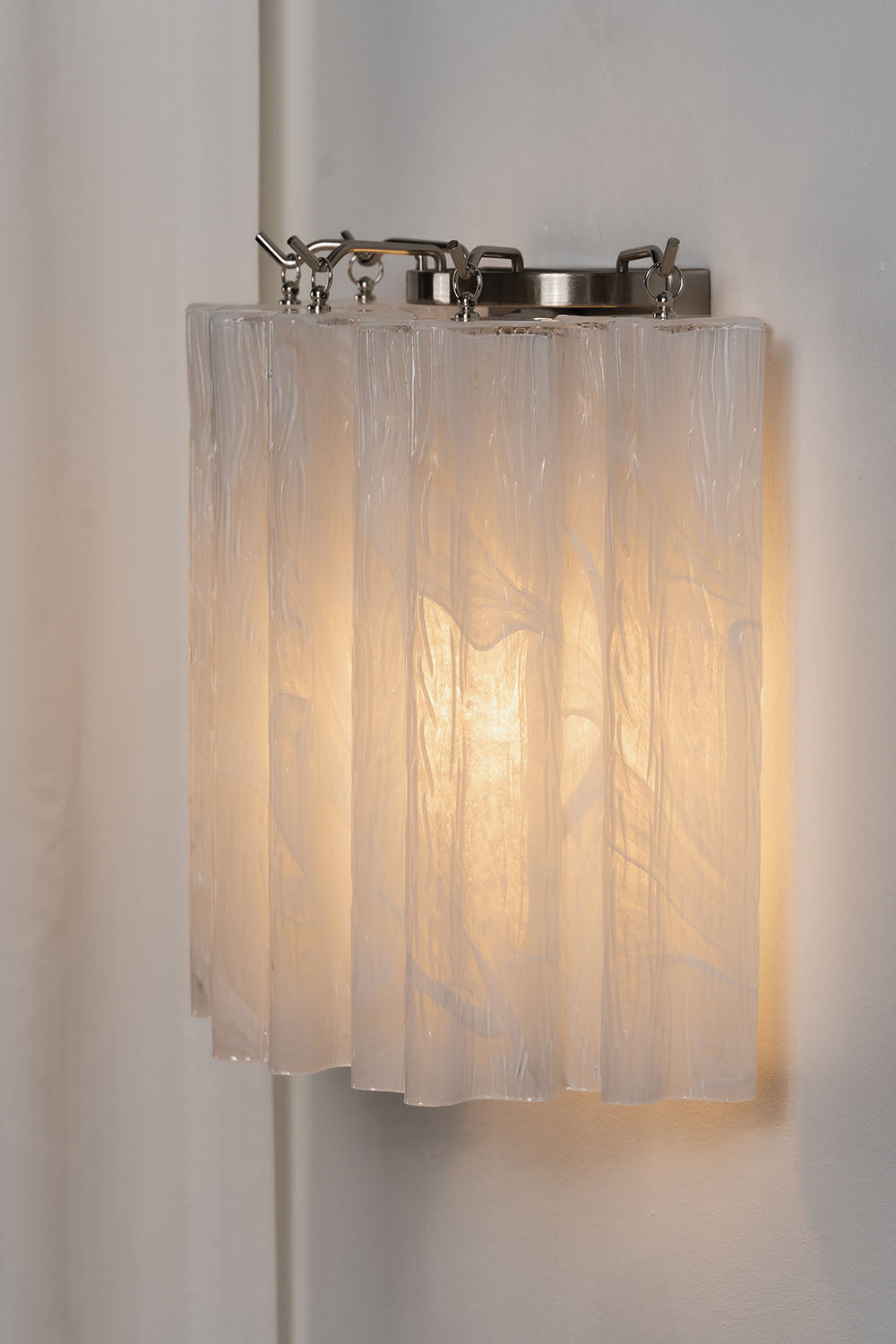 Ysoline Rippled Glass Curtain Sconce Light | Rippled Glass and Metal | Side angle view of the illuminated sconce on a neutral wall | Samu Lamp